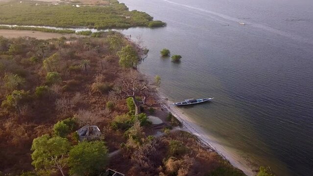Aerial footage of Saloum river delta with mangroves, sandy patches covered in salt and islands with tropical trees and wooden boat nearby, Palmarin, Senegal, descending towards boat while panning.