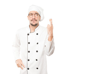 Concerned young chef doing a crossed fingers gesture