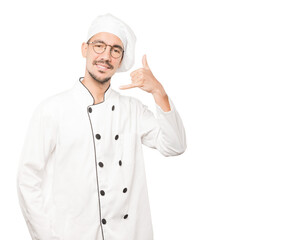 Happy young chef making a gesture of calling with the hand