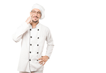 Hesitant young chef making a gesture of being careful with his hand pointing at his eye