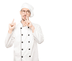 Serious young chef asking for silence gesturing with his finger