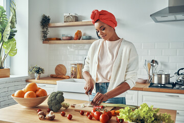 Attractive young African woman cutting veggies at the domestic kitchen