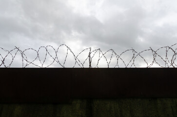 fence barbed wire gray sky clouds danger zone safety passage closed hopelessness decay