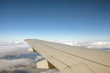 Fototapeta na wymiar the wing of a passenger plane flying in the sky against a blue sky with clouds, copy space