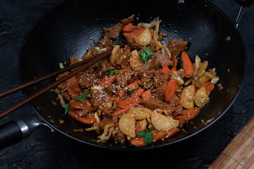 Seitan, daicon and carrot stir fry in wok on black table