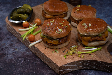 Vegan burgers made with seitan and vegan cheese, pickles on wooden cutting board