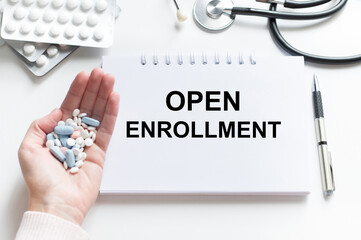 The text open enrollment is written on notepad near a stethoscope on a blue background. Medical...
