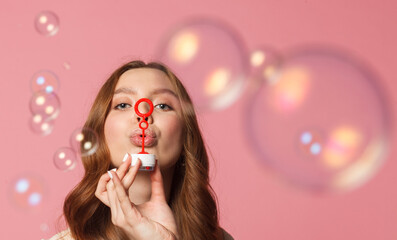 young female model blowing soap bubbles on pink background, close up shot