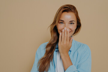 Attractive female hiding mouth while having fun on beige background