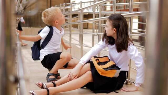 A schoolboy boy in a school uniform sticks to a schoolgirl girl sitting on the floor. Bullying in elementary school.
