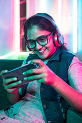 vertical shot of excited girl playing video game on mobile phone with wireless headset while...