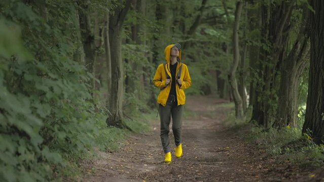 Long shot of woman in yellow jacket and boots walking through the forest, active vacation time