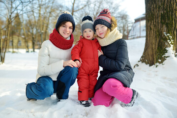 Fototapeta na wymiar Two big sisters and their toddler brother having fun outdoors. Two young girls holding their sibling boy on winter day. Kids during winter break.