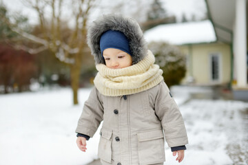 Adorable toddler boy having fun in a backyard on snowy winter day. Cute child wearing warm clothes playing in a snow.