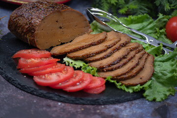 Vegan seitan roast slices with tomato slices on lettuce leaves on slate plate