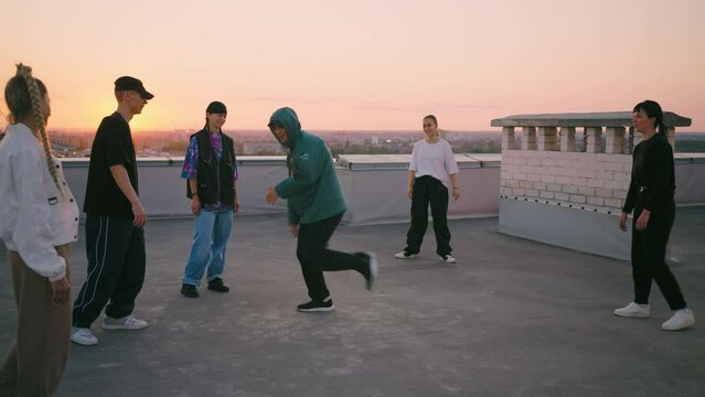 cool breakdancer boy is dancing on roof, young guy in trendy hoody is breaking on floor, friends dance party