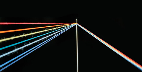 multi-colored threads for sewing in the form of a rainbow pass through an antique needle on a black background