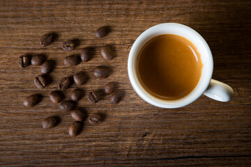 White cup of espresso with coffee beans on wooden background