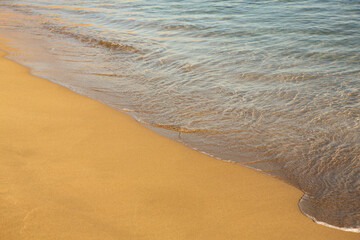Background with golden sand on the coast of the island of Crete. Abstract surface with sand and clear sea water for text.