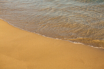 Background with golden sand on the coast of the island of Crete. Abstract surface with sand and clear sea water for text.