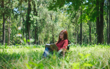 Naklejka na ściany i meble Portrait of a beautiful young asian woman reading a book while sitting on a camping chair in the park