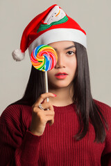 portrait of beautiful young asian woman wearing christmas hat and red dress holding lilipop candy