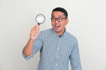 Asian man looking through magnifying glass with surprised expression