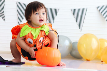 Fototapeta premium Adorable baby girl kid dressing up in orange fancy Halloween pumpkin costume, cheerful little cute child go to party, playing trick or treat, Happy Halloween celebration.