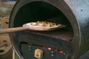 fresh pizza on a wooden slide is pushed into a self-made recycling oven built from an old metal...