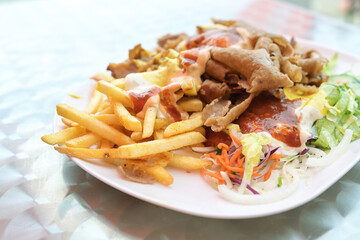 Doner kebab on a plate with French fries, salad and various sauces on a plate, popular fast food from Turkish cuisine, copy space, selected focus