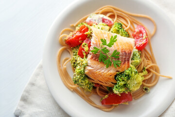 Wild salmon fillet on whole grain spaghetti with broccoli, tomatoes and parsley garnish, healthy meal on a white plate, copy pace, high angle view from above, selected focus