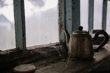 An old teapot in a cobweb on a dirty table by the window of an abandoned house
