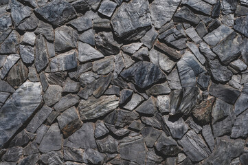 Stone masonry wall, rough layered black sandstone, uneven grungy vintage background close-up, grunge texture