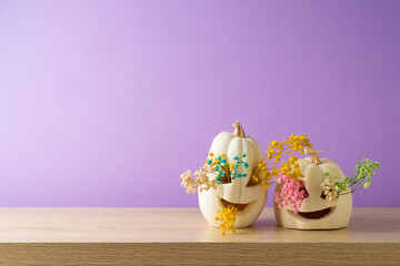 Halloween holiday creative concept with white pumpkin jack o lantern and dried flowers on wooden table over purple background