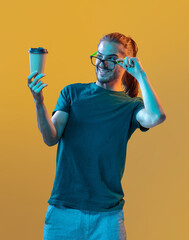 Young handsome guy in glasses with a glass of coffee on a colored background
