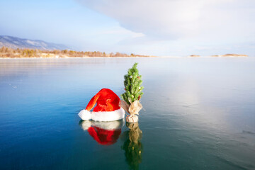 Christmas tree with toys and Santa Claus hat on the transparent ice of Lake Baikal. Happy New Year and Merry Christmas.