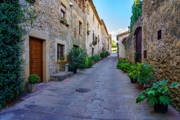 Beautiful alley with old stone houses and pots on the street with plants and flowers, Monells, Girona, Catalonia.