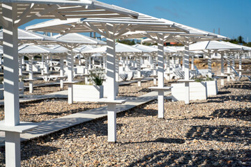 Fototapeta na wymiar Rows of wooden umbrellas from the sun on the seashore in the morning. Wooden paths on the sand between umbrellas. Beach holiday at the resort.
