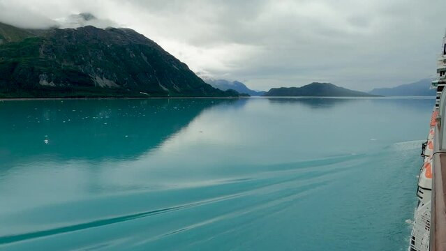View side of cruise ship making gentle ripples in beautiful clear smooth water of Glacier Bay on overcast day