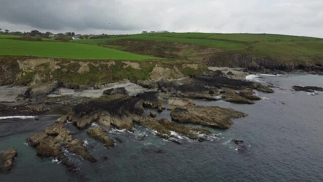 Green fields on a rocky seashore in southern Ireland. The waters of the Celtic Sea hit the coastal rocks. Seashore, landscape.