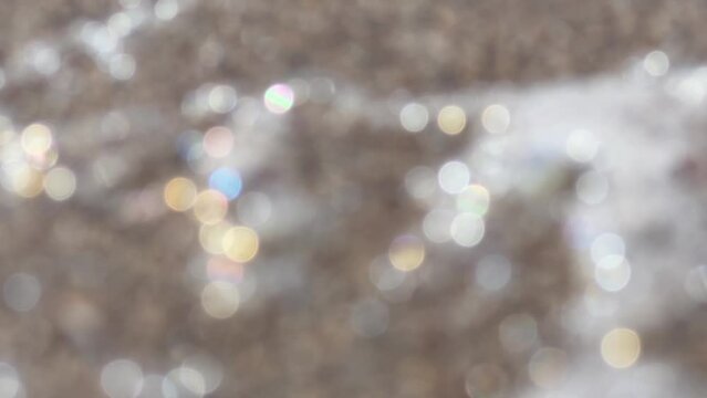 Beautiful defocused abstract background with sparkling shimmer in rainbow colors. Wallpaper with bokeh blur of sea foam on sand. Defocused shiny glitter. Film grain. Soft focus. Live camera. Blur