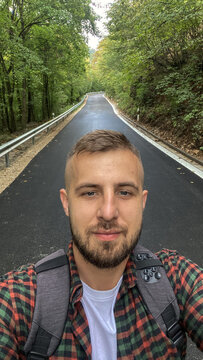 A guy takes a selfie on a scenic forest road.
