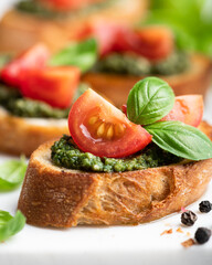 Pesto bruschetta with cherry tomatoes and basil on white background, selective focus