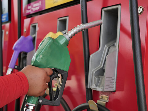 man hand holding a green gas nozzle. A man's hand is pulling the fuel dispenser out of the red meter cabinet. E20 uses a green fuel nozzle. Woman is holding a gasoline fuel pistol at gas station.