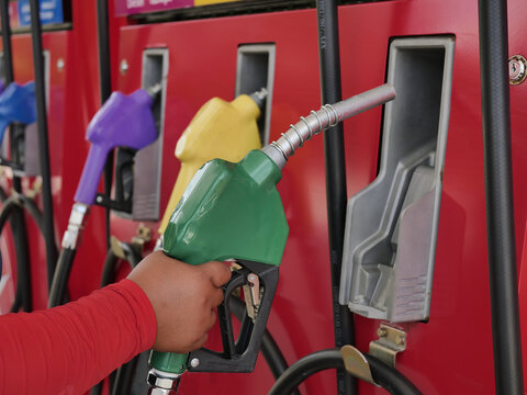 female hand holding a green gas nozzle. A woman's hand is pulling the fuel dispenser out of the red meter cabinet. E20 uses a green fuel nozzle. Woman is holding a gasoline fuel pistol at gas station.