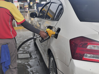 Fototapeta premium Dispenser pumping in car at gas station. Hand holding yellow fuel pump nozzle and refilling car. Woman refueling car at self service gas station. Hand refilling the car with fuel, focus hand.