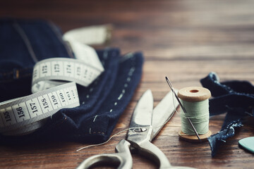 Shortening jeans. Measuring tape, scissors, spools of thread and chalk on wooden table. Jeans cutting. - 529679769
