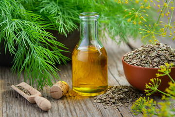 Bottle of dill seeds oil, bunch of fresh green dill and bowl of dried fennel seeds on wooden board. Alternative herbal medicine. Useful seasoning for cooking. - obrazy, fototapety, plakaty