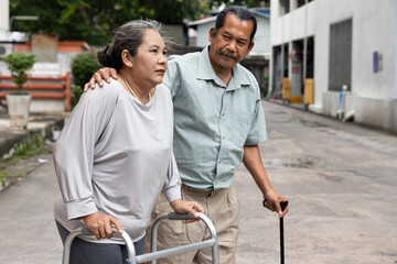 Senior wife with knee or leg injury, using walking aid with supporting old husband, concept of...