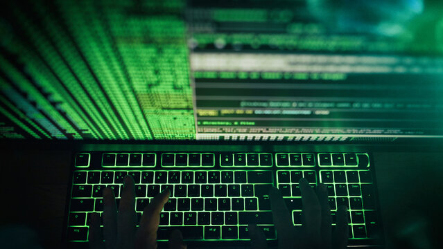 Hände von Computerhacker auf Tastatur vor Bildschirm mit Code
